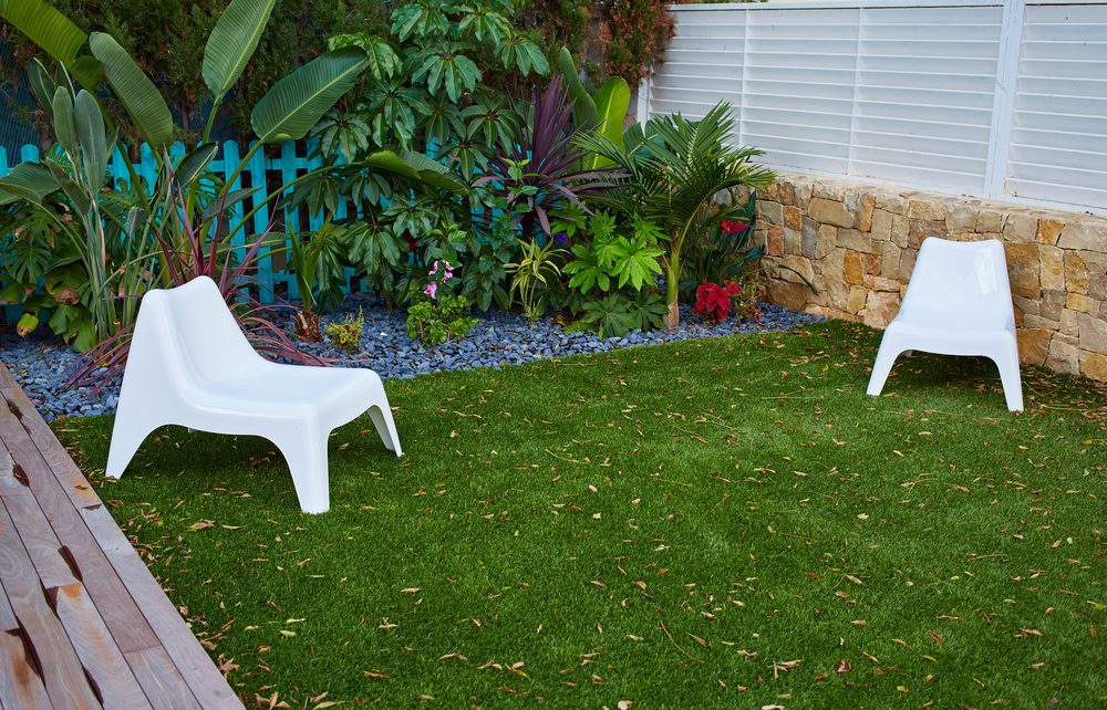 Artificial grass in a backyard with modern chairs and lush plants.