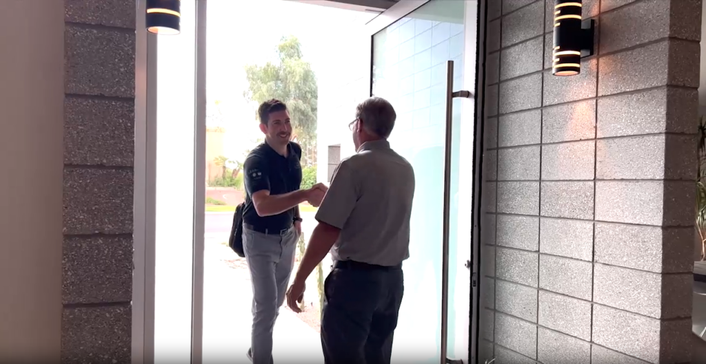 Two men shaking hands at the entrance, discussing artificial turf installation.