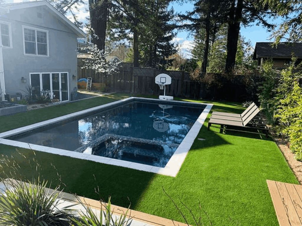 Artificial grass surrounding a backyard pool with a basketball hoop and lounge chairs.