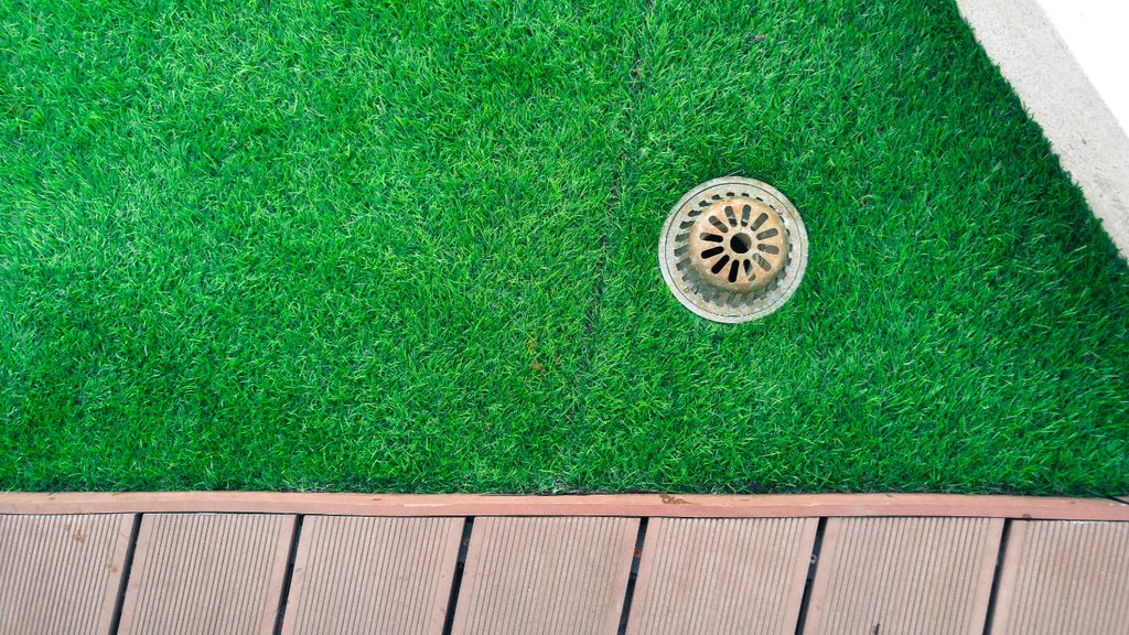 Close-up of synthetic turf with drainage grate in Arizona luxury lawn.