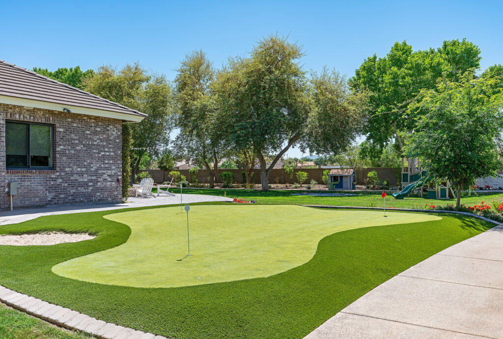 Artificial grass putting green in a backyard with trees and a house.