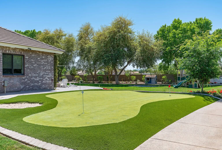 Artificial grass putting green in a backyard with trees and a house.