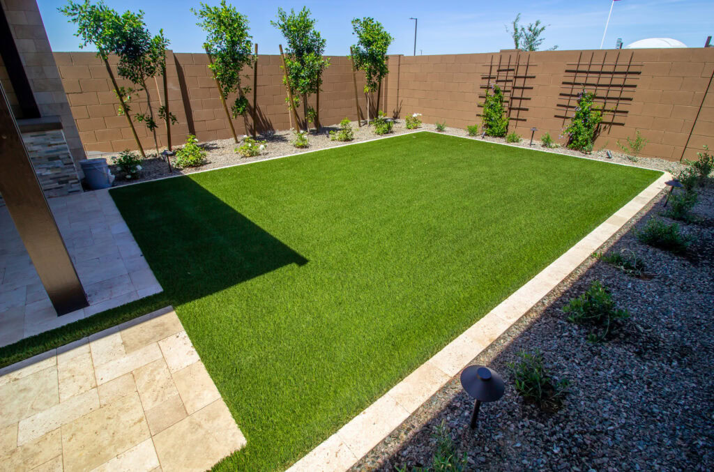 Artificial grass lawn with trees and a privacy fence in a backyard.