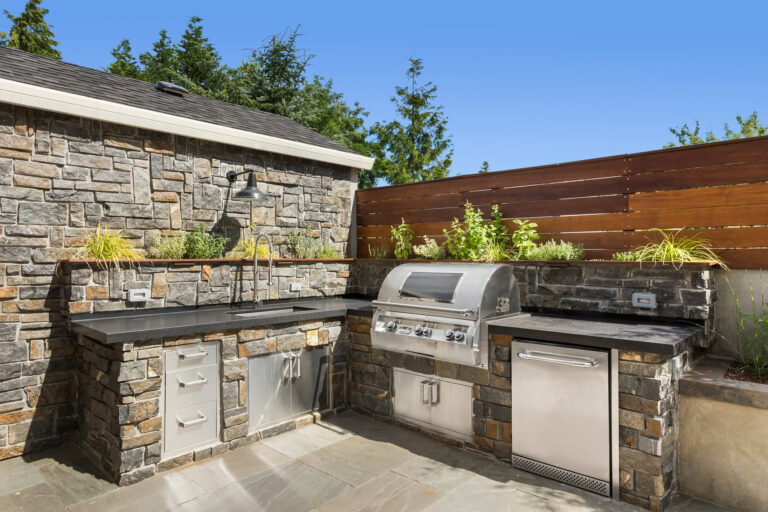 Outdoor kitchen with stone countertops, built-in grill, and storage cabinets in a backyard.