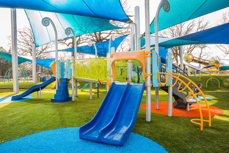 Children's playground with slides and shade sails over artificial turf in Arizona.