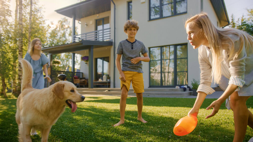 Kids and dog playing on artificial turf in backyard.