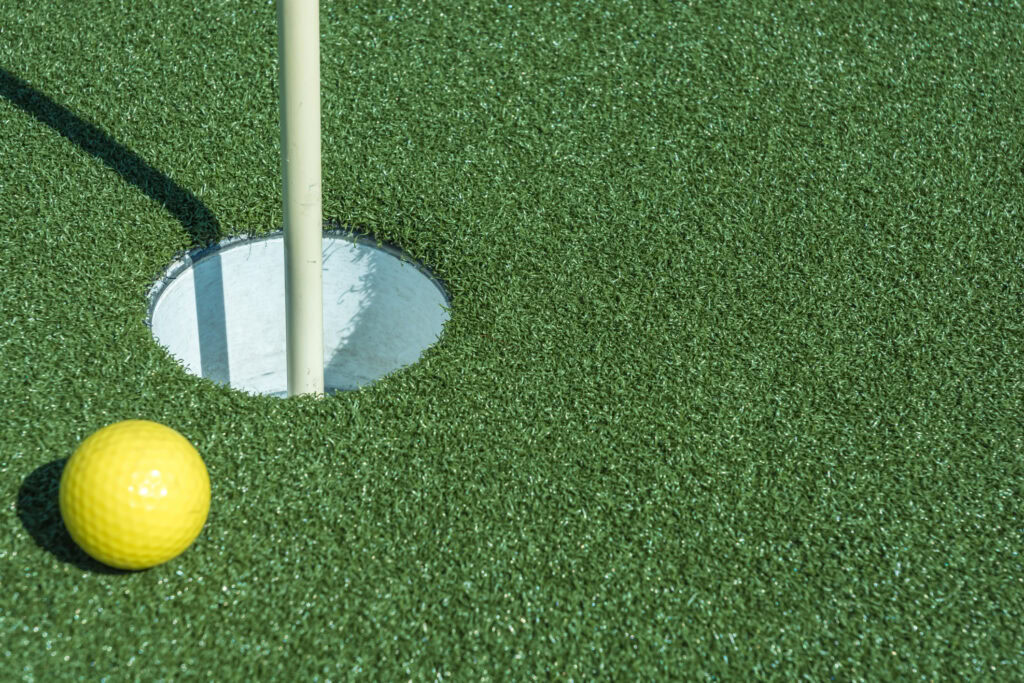 Close-up of artificial grass putting green with golf ball and hole.