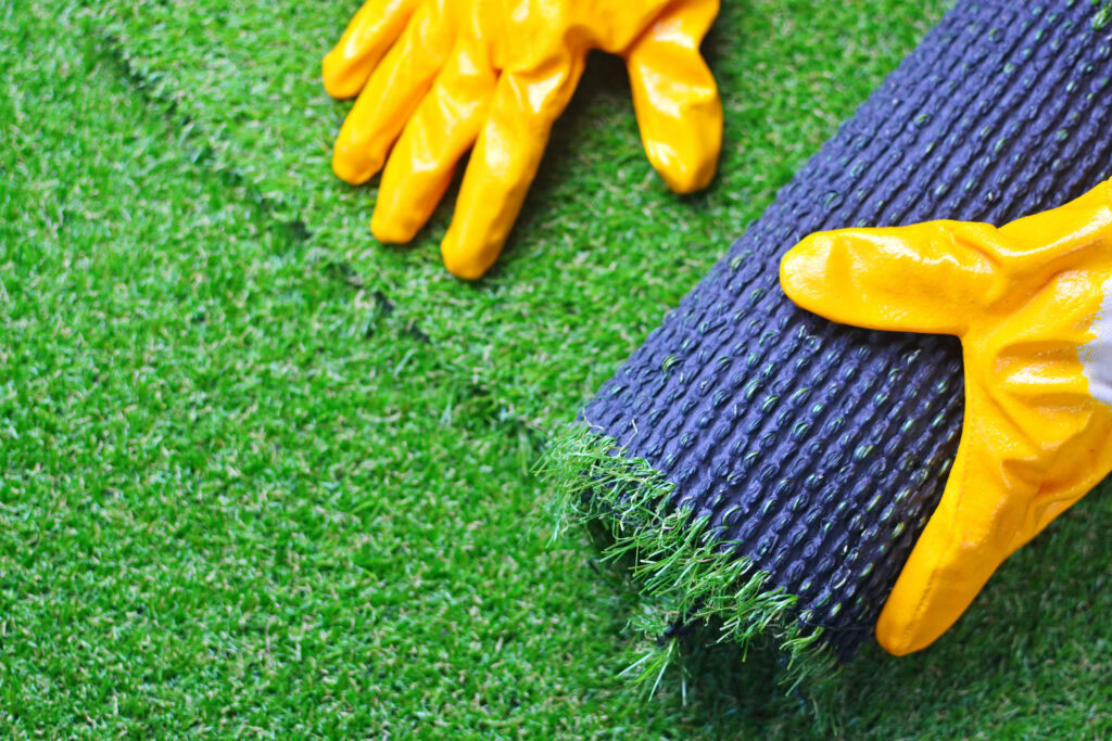 Installing synthetic turf with yellow gloves on a green yard.