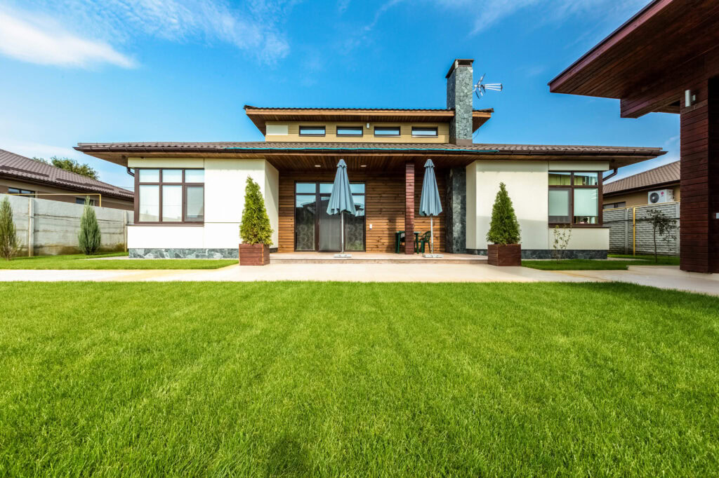 Modern house with lush green synthetic grass yard and outdoor seating area.