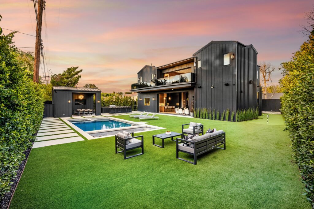Luxury backyard with pool, modern house, and well-maintained lawn at sunset.
