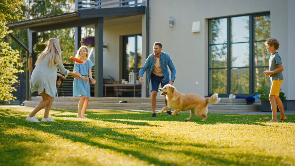 Family playing with dog on lush pet-friendly turf in backyard.