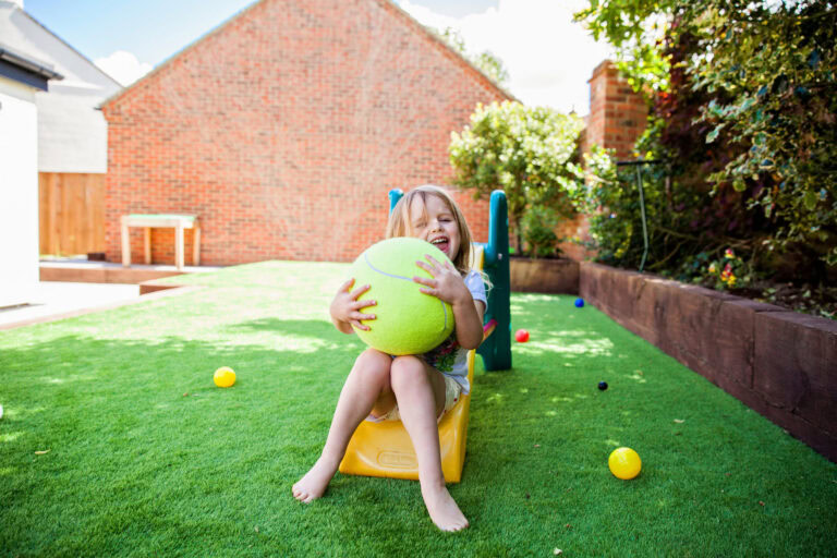 Child enjoying outdoor play on artificial turf with a large ball in Arizona backyard.