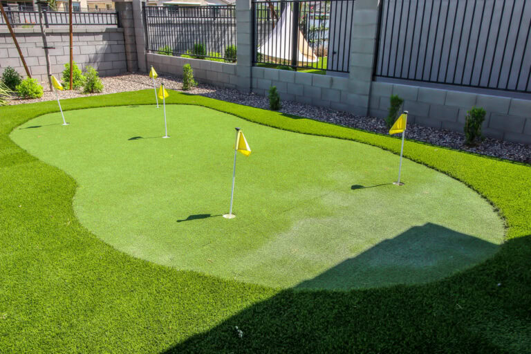 Artificial turf putting green with flags in a backyard setting.