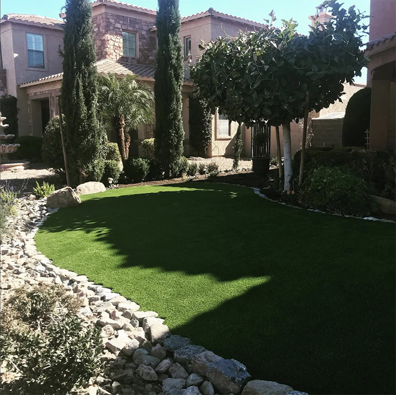 Beautiful landscaped backyard with lush green putting green and trees.