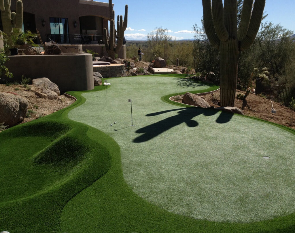 Luxury multi-hole backyard putting green surrounded by towering saguaro cactus, granite boulders, and sweeping desert valley view, Scottsdale Arizona