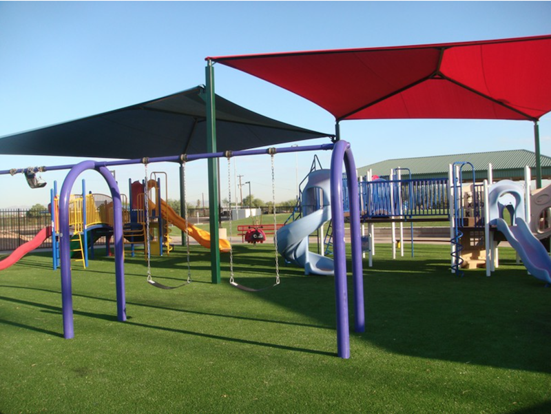 Colorful playground with slides, swings, and shade sails on a lush green lawn.