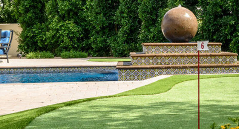Close-up of backyard putting green hole 6 flagstick with pool and ornate Talavera tile fountain water feature, Scottsdale Arizona
