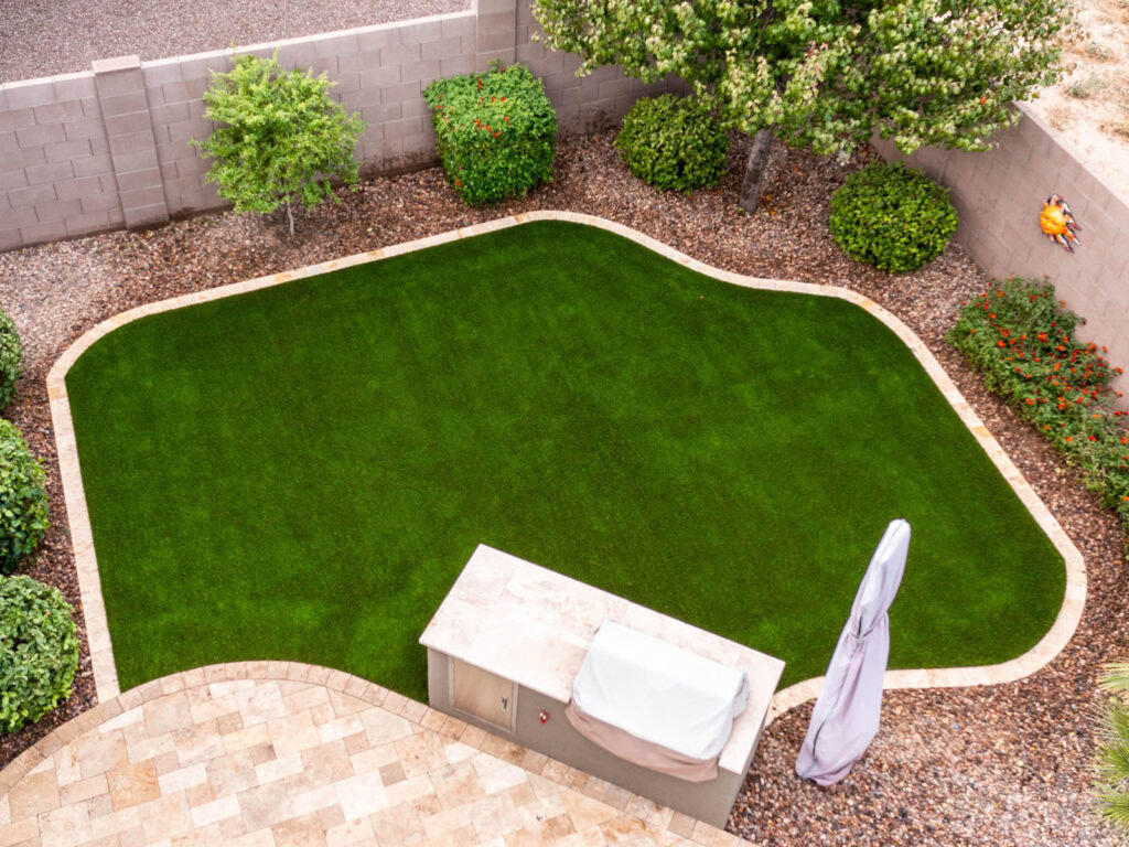 Aerial view of residential backyard with organic curved artificial turf, built-in BBQ island, and paver patio, block wall fence, Arizona