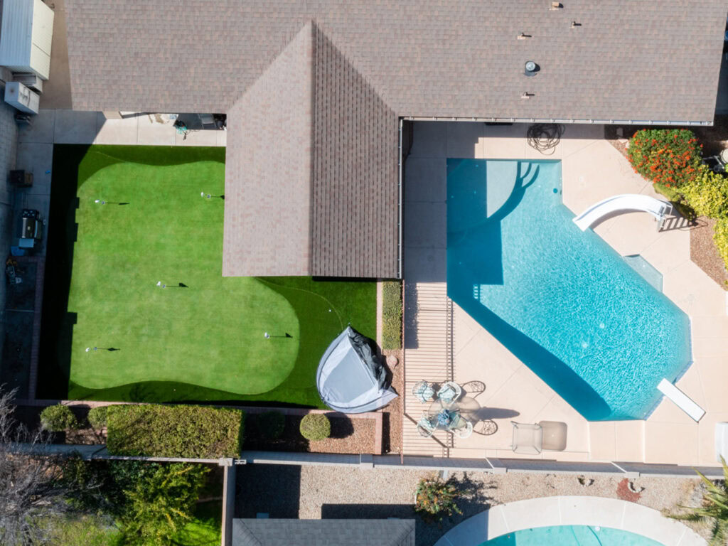 Aerial view of backyard 4-hole putting green adjacent to rectangular swimming pool, lounge chairs, and suburban home, Arizona