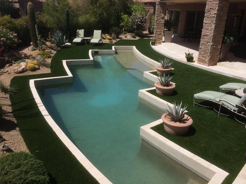 Luxury organic-shaped pool with artificial turf extending to pool edge, stone column covered patio, lounge chairs, cactus, and terracotta pot agave plants, Scottsdale Arizona