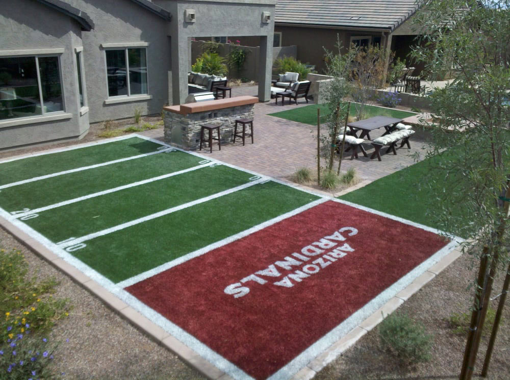 Custom backyard miniature football field with Arizona Cardinals red and green artificial turf, yard lines, end zone lettering, outdoor bar with stools, and patio seating
