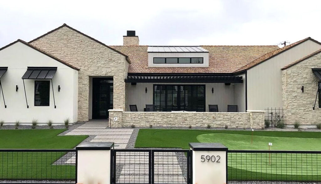 Modern house with lush green lawn and putting green in front yard.