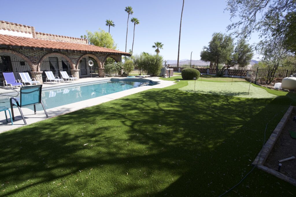 Large backyard artificial lawn with putting green, swimming pool, and Spanish-style home with Arizona mountain views