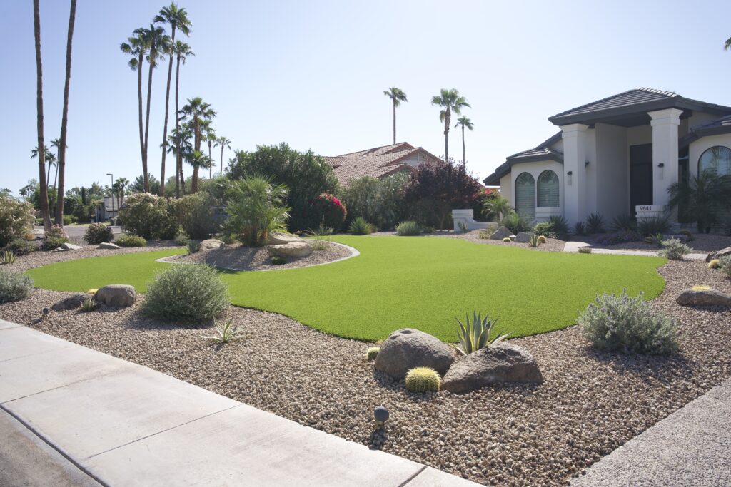 Residential front yard with artificial turf island, desert plants, boulders, and palm trees in Scottsdale Arizona