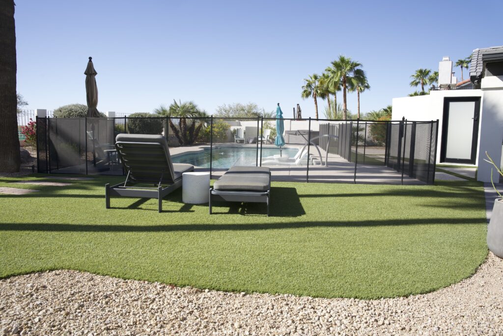 Pool surround with lush artificial turf, modern chaise lounges, and pool fence at Scottsdale Arizona home