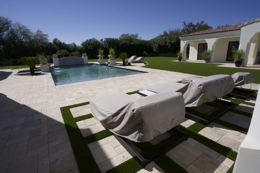 Artificial turf inlays between travertine pavers at luxury Scottsdale pool deck with covered lounge chairs