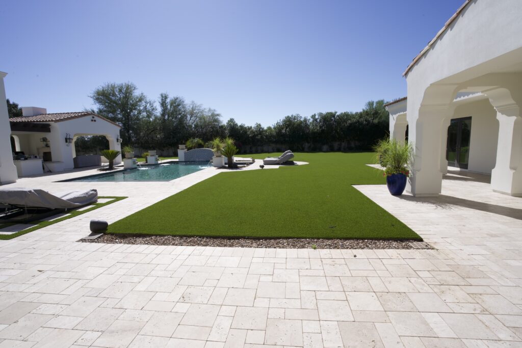 Luxury Scottsdale estate with artificial grass adjacent to pool, travertine paver patio, and white stucco architecture