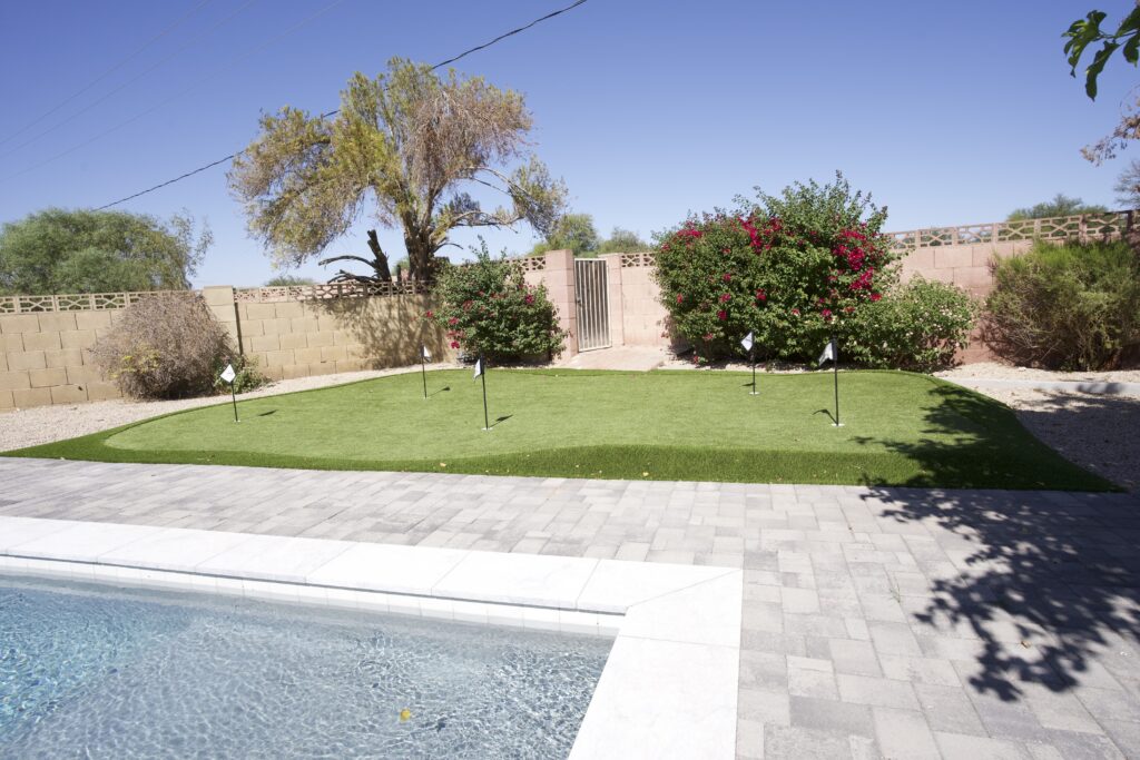 Backyard putting green with four holes and flags, blooming bougainvillea, and adjacent pool in Arizona