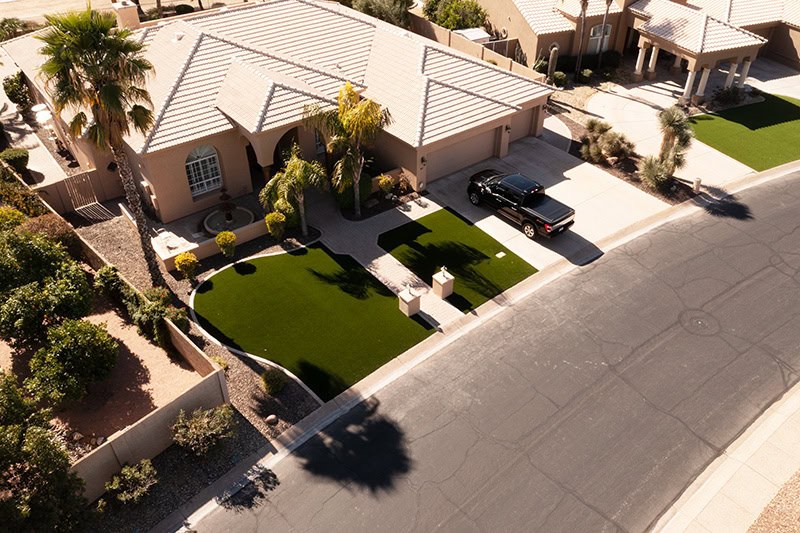 Aerial drone view of an Arizona home with a lush artificial turf front lawn and curved paver driveway