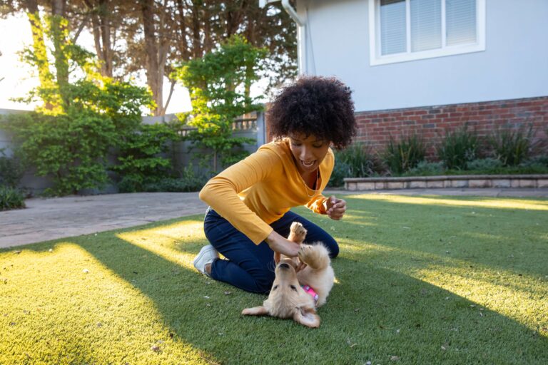Woman playing with a puppy on artificial grass in backyard.